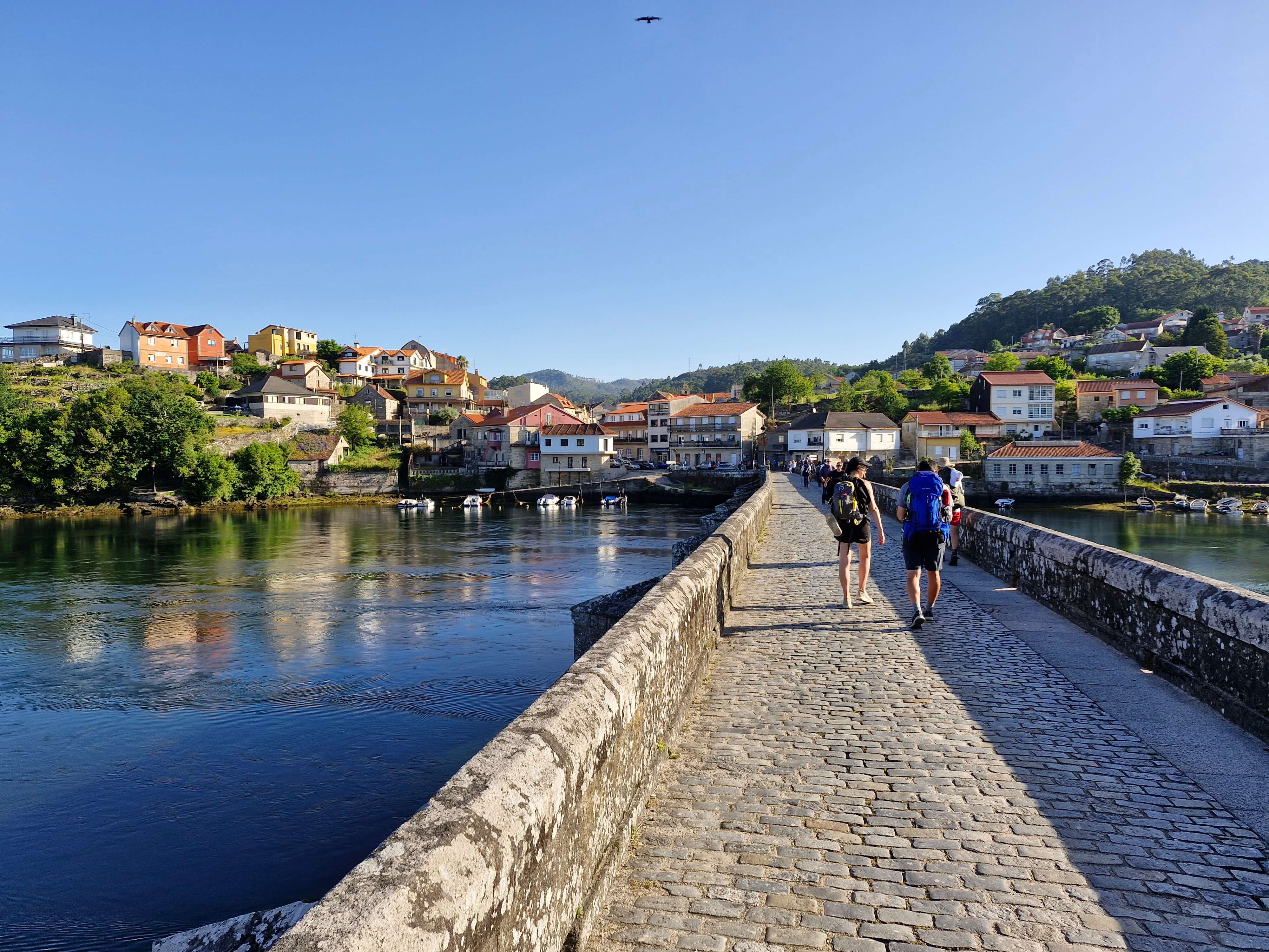 Camino Portuguese - hikers cross medieval bridge ponte sampaio pontevedra